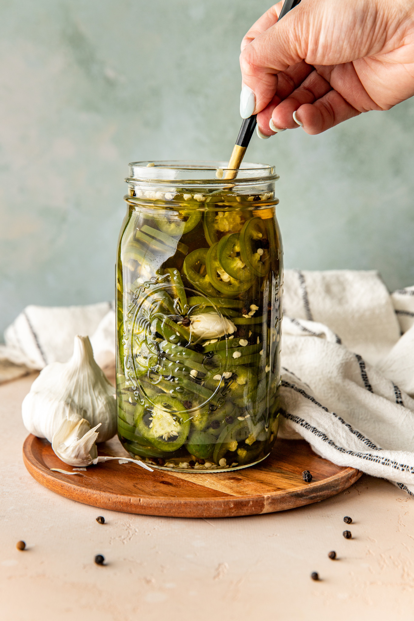a hand picking out pickled jalapeños with a fork out of a mason jar.