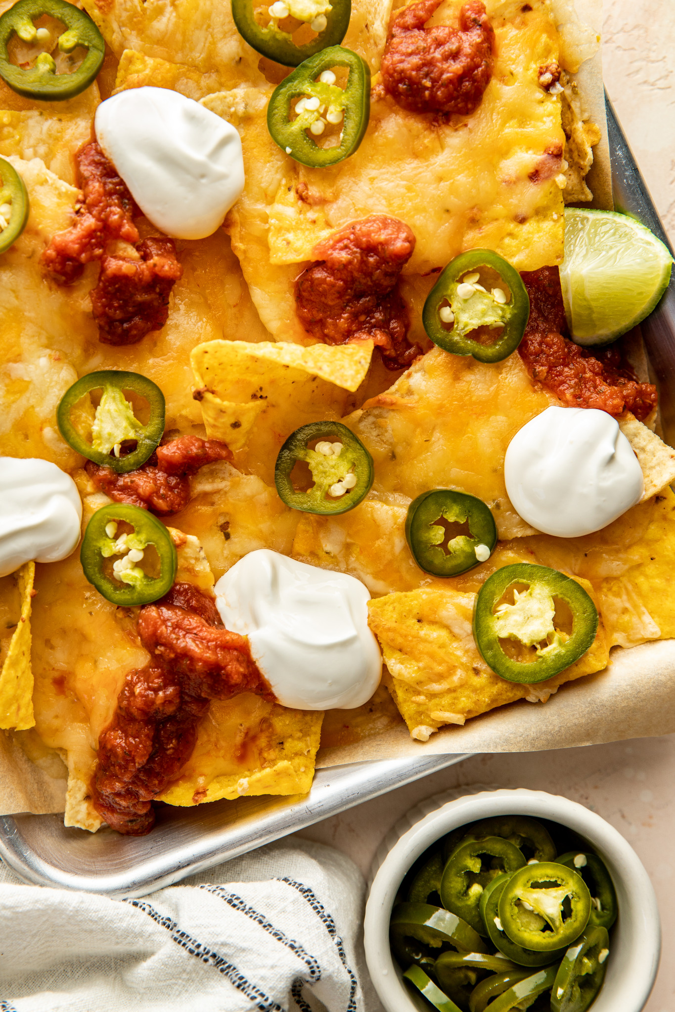 a sheet pan of nachos with pickled jalapenos, sour cream, cheese, and salsa.