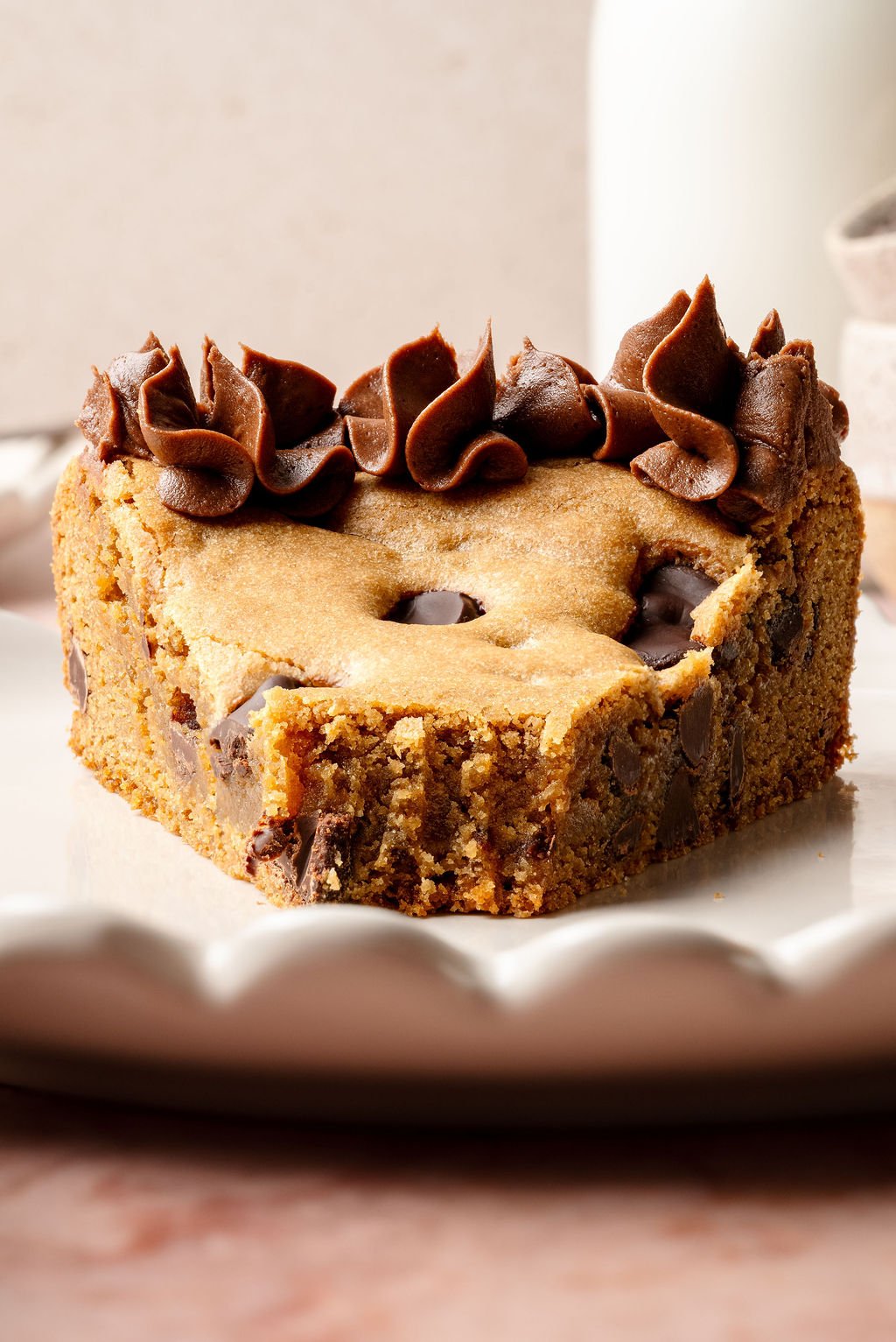 Close-up of a partially eaten slice of chocolate chip cookie cake with piped chocolate frosting, showing a moist and chewy center filled with chocolate chips.