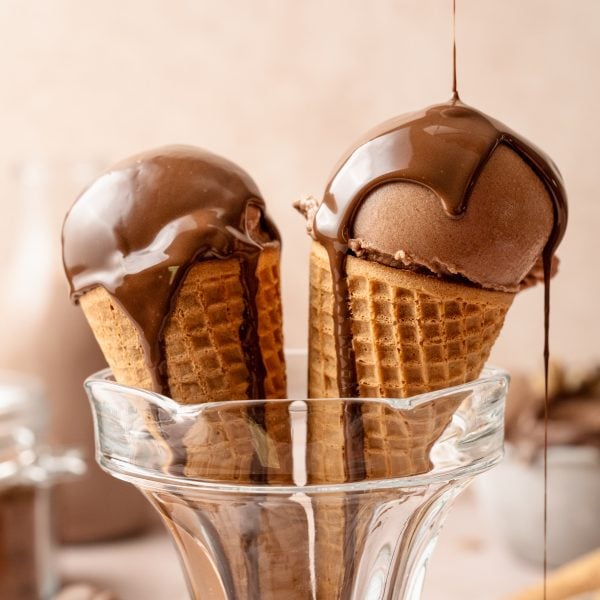 Two chocolate ice cream cones in glass cup being topped with chocolate magic shell.