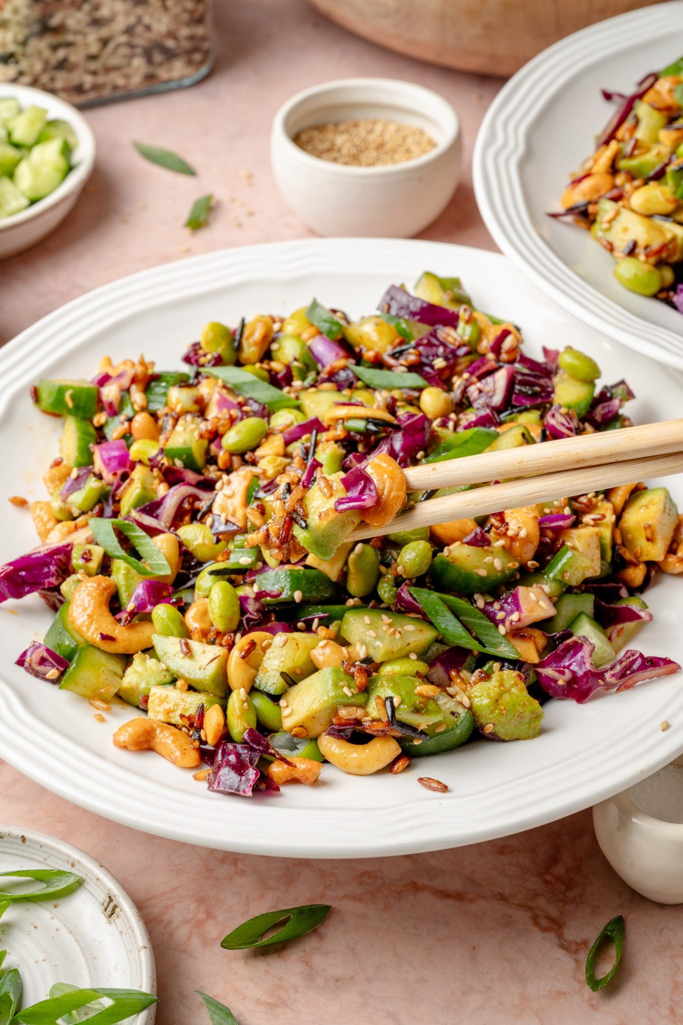 White plate filled with a serving of crispy rice salad, highlighting the colorful mix of avocado, cucumbers, cashews, and red cabbage, with chopsticks and sesame seeds in the background.