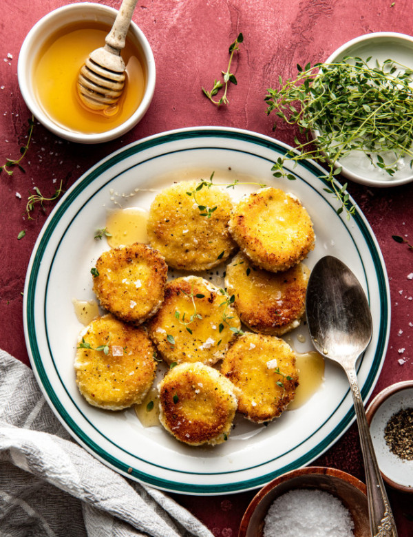 Fried goat cheese croutons on plate drizzled with honey and spoon on plate.