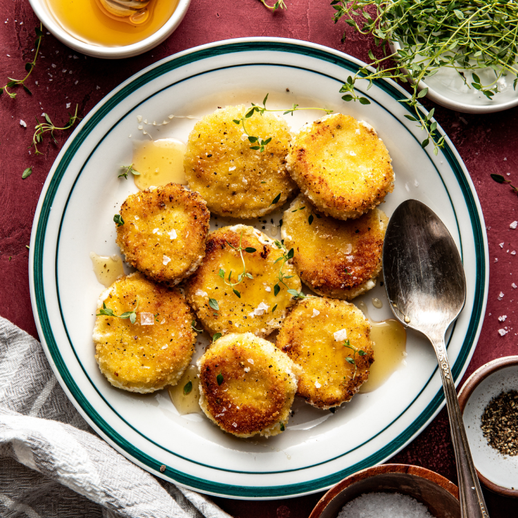 Fried goat cheese drizzled with honey on plate with spoon.