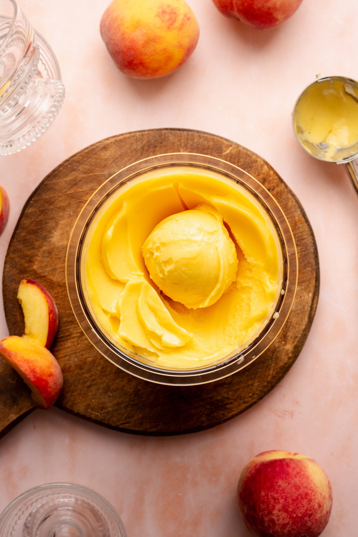 Peach sorbet in ninja creami pint container scooped in container on top of wood cutting board with peaches on the side of the board and on the table.