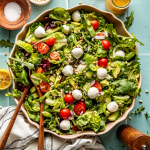 Favorite everyday salad tossed in large ceramic bowl with wooden spoons.