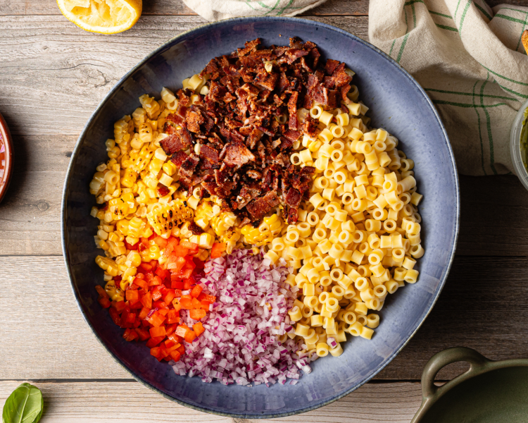 Pasta salad ingredients added to large blue bowl.