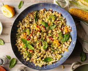 Chilled pesto pasta salad in large blue serving bowl topped with fresh basil.