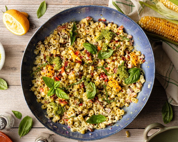 Chilled pesto pasta salad in large blue serving bowl topped with fresh basil.