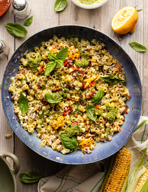 Sweet corn pesto pasta salad tossed together in large blue serving bowl and garnished with fresh basil.