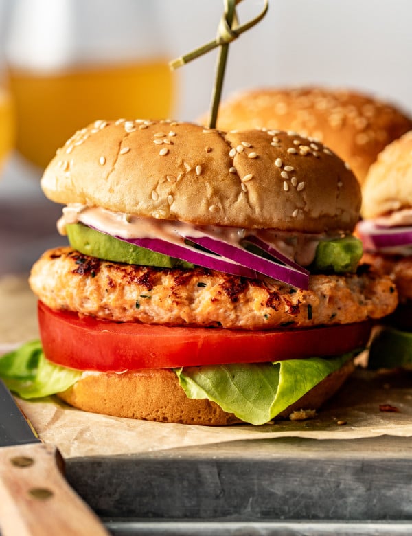 Chicken burger on burger bun with toppings and toothpick in the middle holding it together.