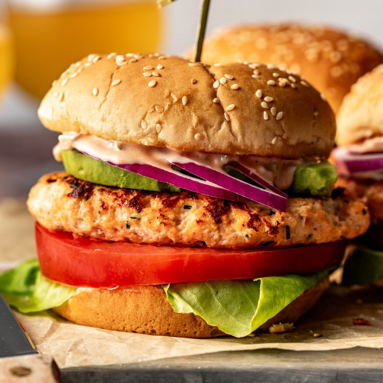 Chicken burger on burger bun with toppings and toothpick in the middle holding it together.