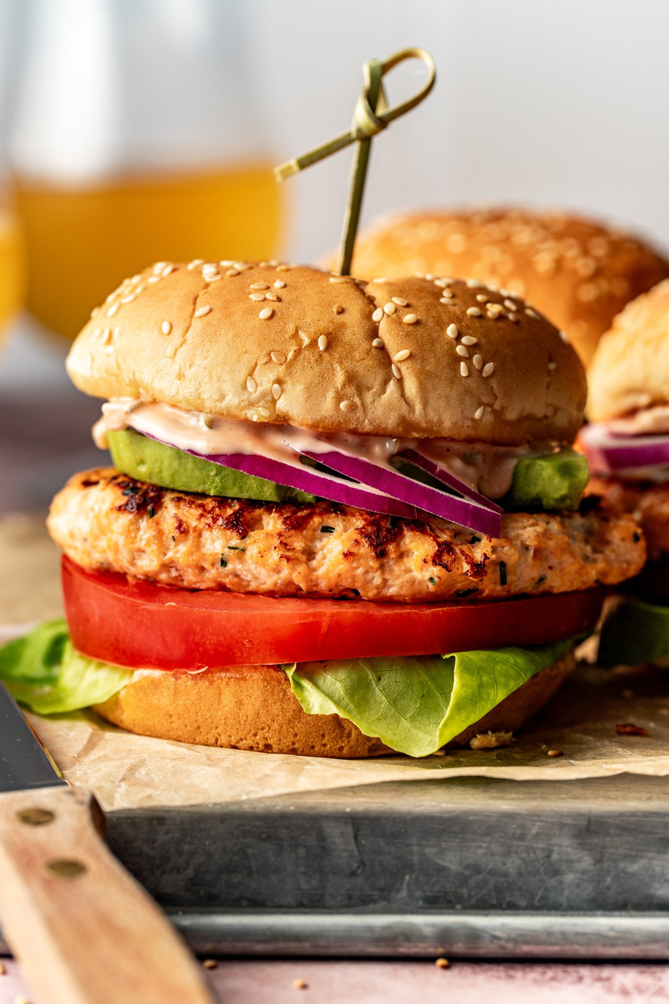 Chicken burger on burger bun with toppings and toothpick in the middle holding it together.
