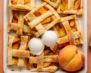 Sliced peach slab pie bars in the baking dish, served with scoops of vanilla ice cream and a whole peach for garnish. The bars are golden, crisp, and ready to enjoy.