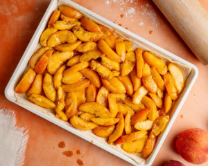 Overhead view of the baking dish filled with the prepared peach filling, evenly distributed over the bottom layer of puff pastry.
