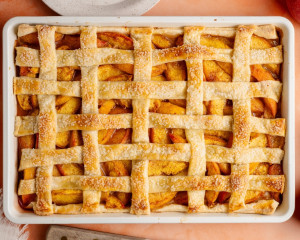 Fully baked peach slab pie with a golden brown, flaky lattice crust sprinkled with coarse sugar. The peach filling is bubbly and caramelized at the edges.