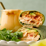 Upclose image of inside of creamy chipotle chicken wrap with jar of chipotle mayo behind it.