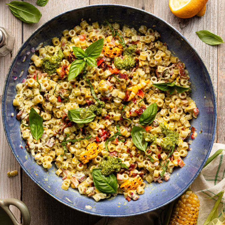 Chilled sweet corn pesto pasta salad in large blue serving bowl topped with fresh basil.