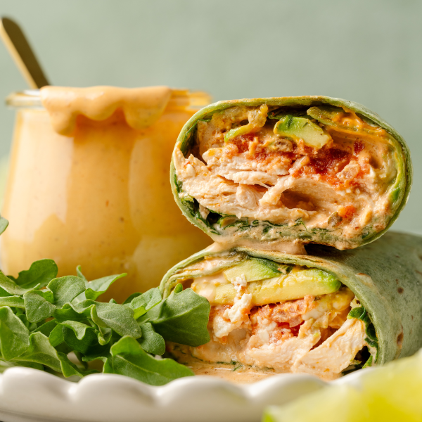 Upclose image of inside of creamy chipotle chicken wrap with jar of chipotle mayo behind it.