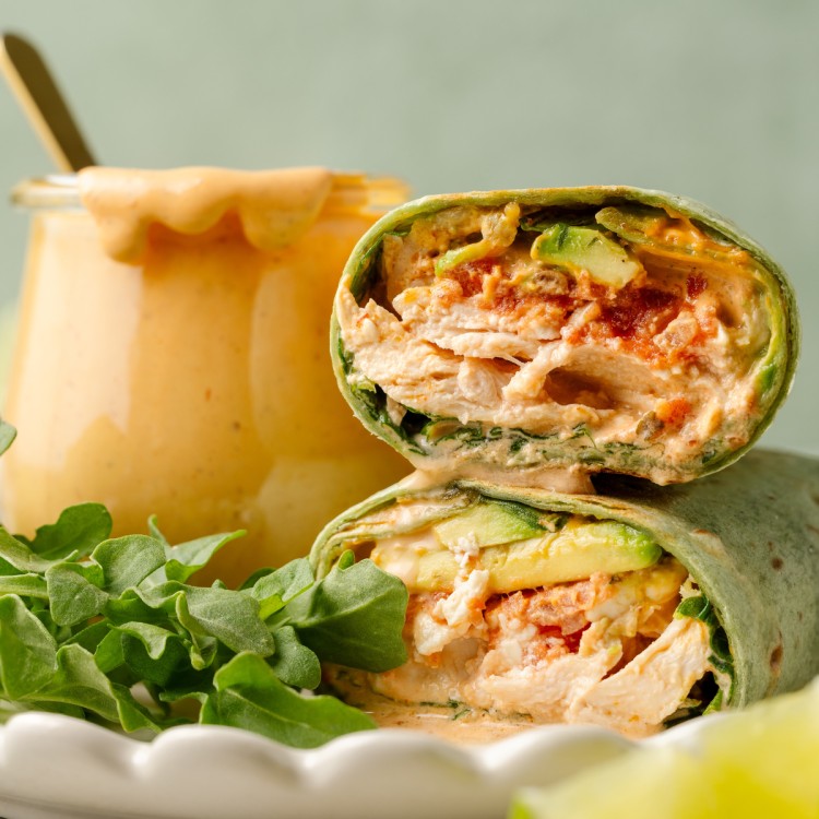 Upclose image of inside of creamy chipotle chicken wrap with jar of chipotle mayo behind it.