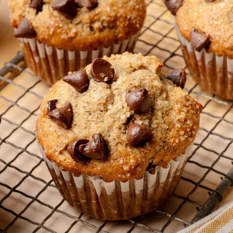 Upclose shot of 3 banana chocolate chip muffins cooling on wire rack.