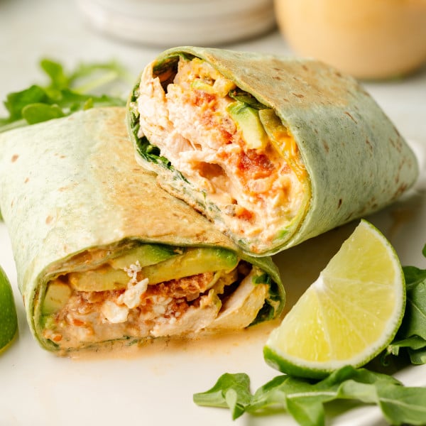 Chipotle chicken wrap sliced in half and stacked on plate with arugula and lime garnish on plate.