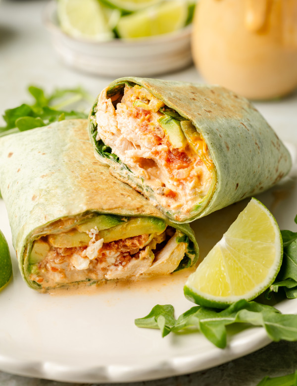 Chipotle chicken wrap sliced in half and stacked on plate with arugula and lime garnish on plate.