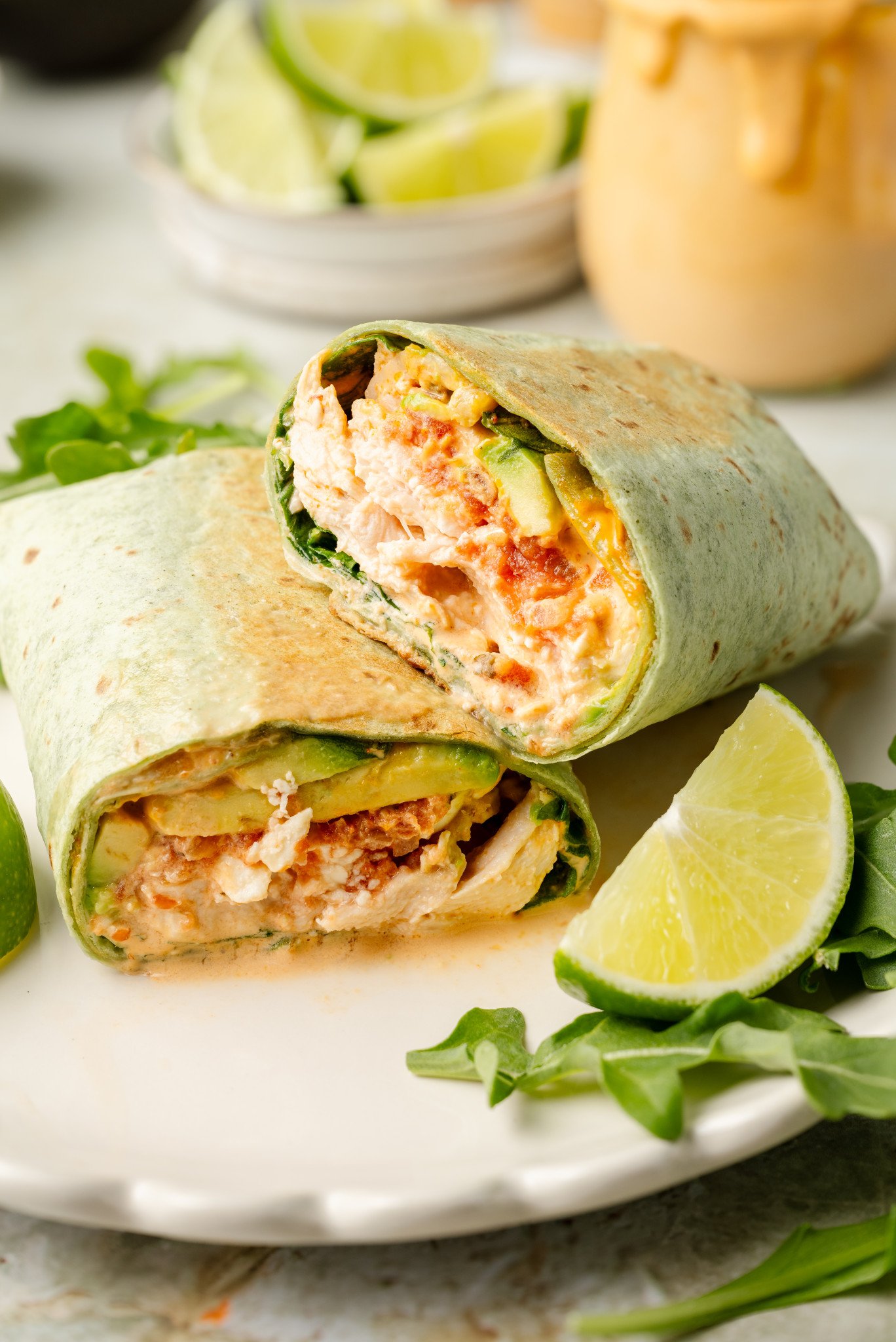 Chipotle chicken wrap sliced in half and stacked on plate with arugula and lime garnish on plate.