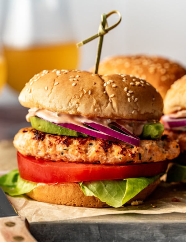 Chicken burger on burger bun with toppings and toothpick in the middle holding it together.