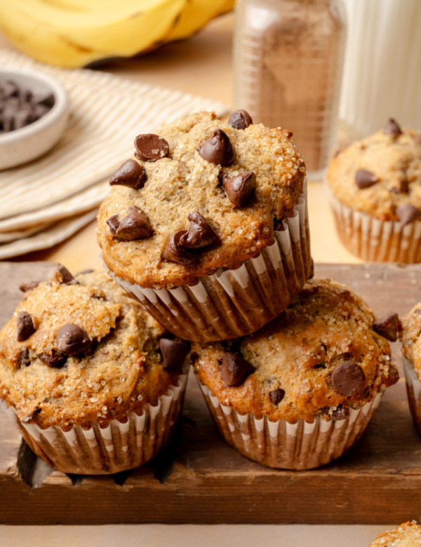 Three chocolate chip banana muffins stacked together on wood board.
