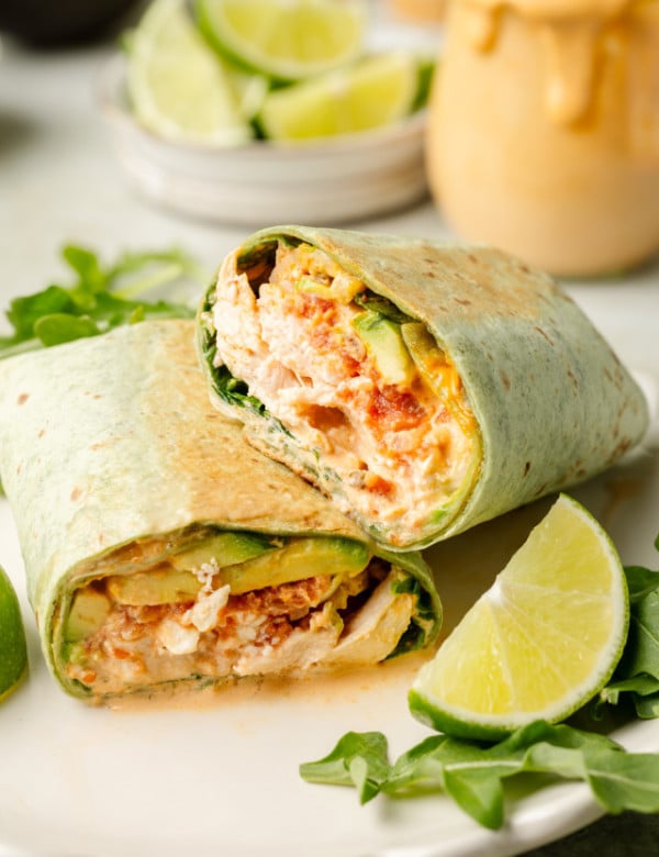 Chipotle chicken wrap sliced in half and stacked on plate with arugula and lime garnish on plate.