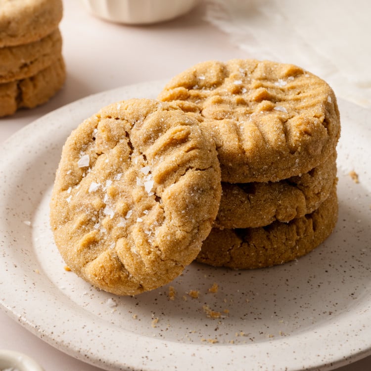 A stack of three peanut butter cookies on a plate with a fourth cookie stacked vertically against them.