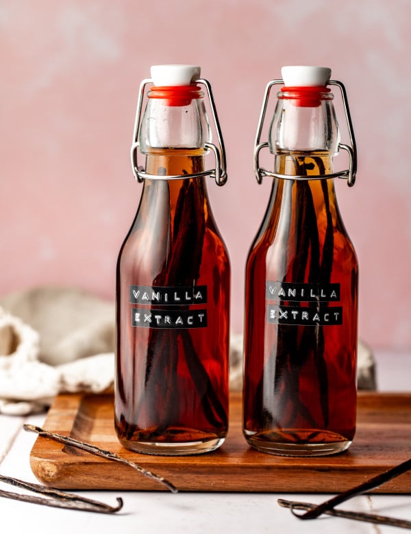 Homemade vanilla extract bottles on wood cutting board.