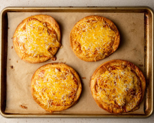 Baked Mexican pizzas on a parchment-lined baking sheet. The cheese is melted and lightly browned, some bubbling over the crispy edges.