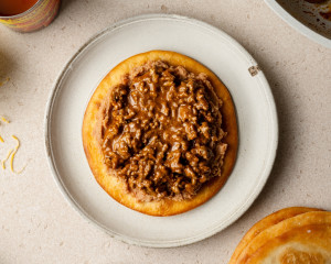 The refried bean layer is now topped with a generous amount of saucy ground beef, creating the second layer of the Mexican pizza.