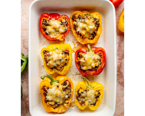 Baked quinoa stuffed bell peppers in a white baking dish, topped with melted golden-brown cheese and ready to serve.