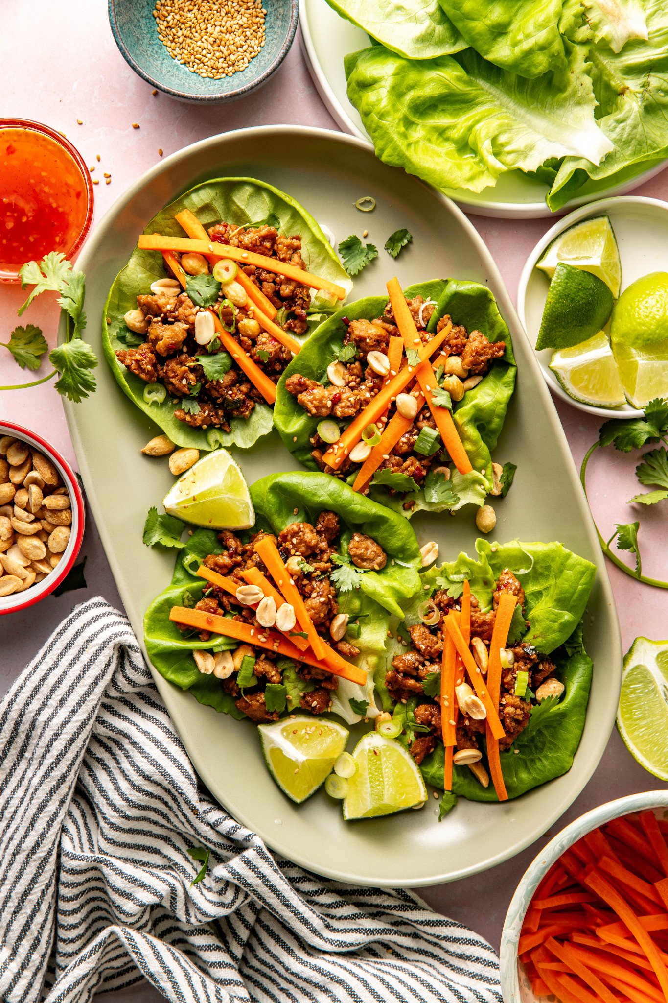 Four Thai chicken lettuce wraps on large oval plate garnished with pickled carrots, peanuts and lime wedge.