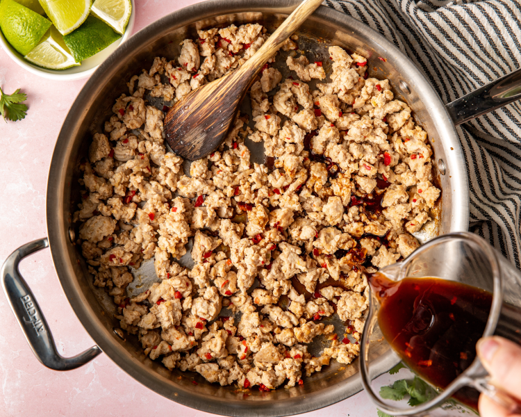Adding sauce to cook ground chicken in large skillet.