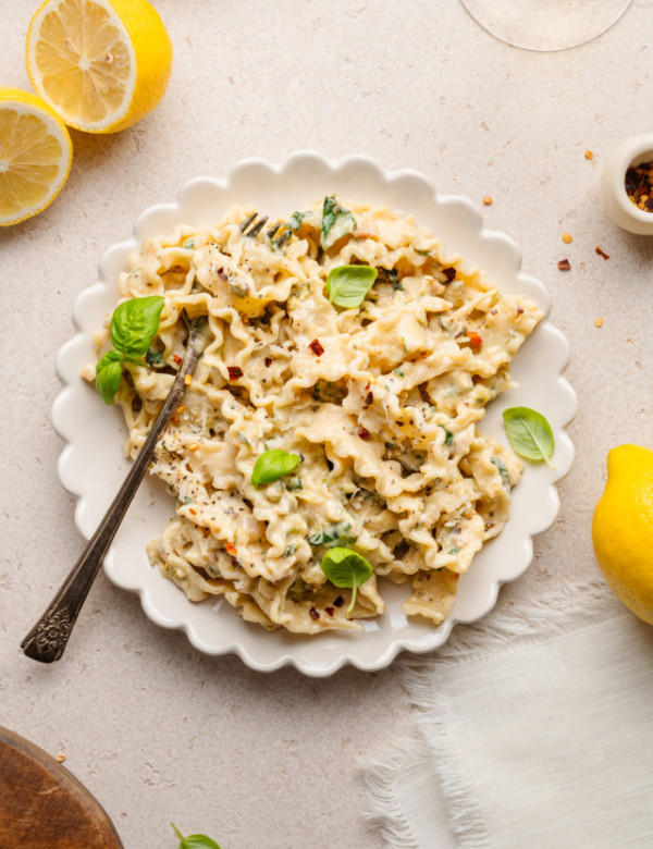 Zucchini lemon pasta garnished with basil in white scalloped bowl with fork.