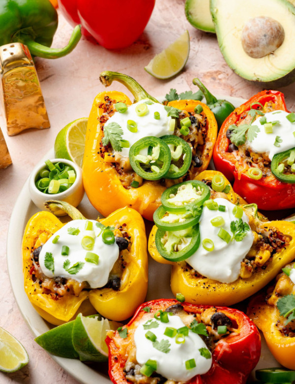 Top view of red and yellow bell peppers stuffed with cheesy quinoa and topped with dollops of sour cream, jalapeños, and fresh herbs.