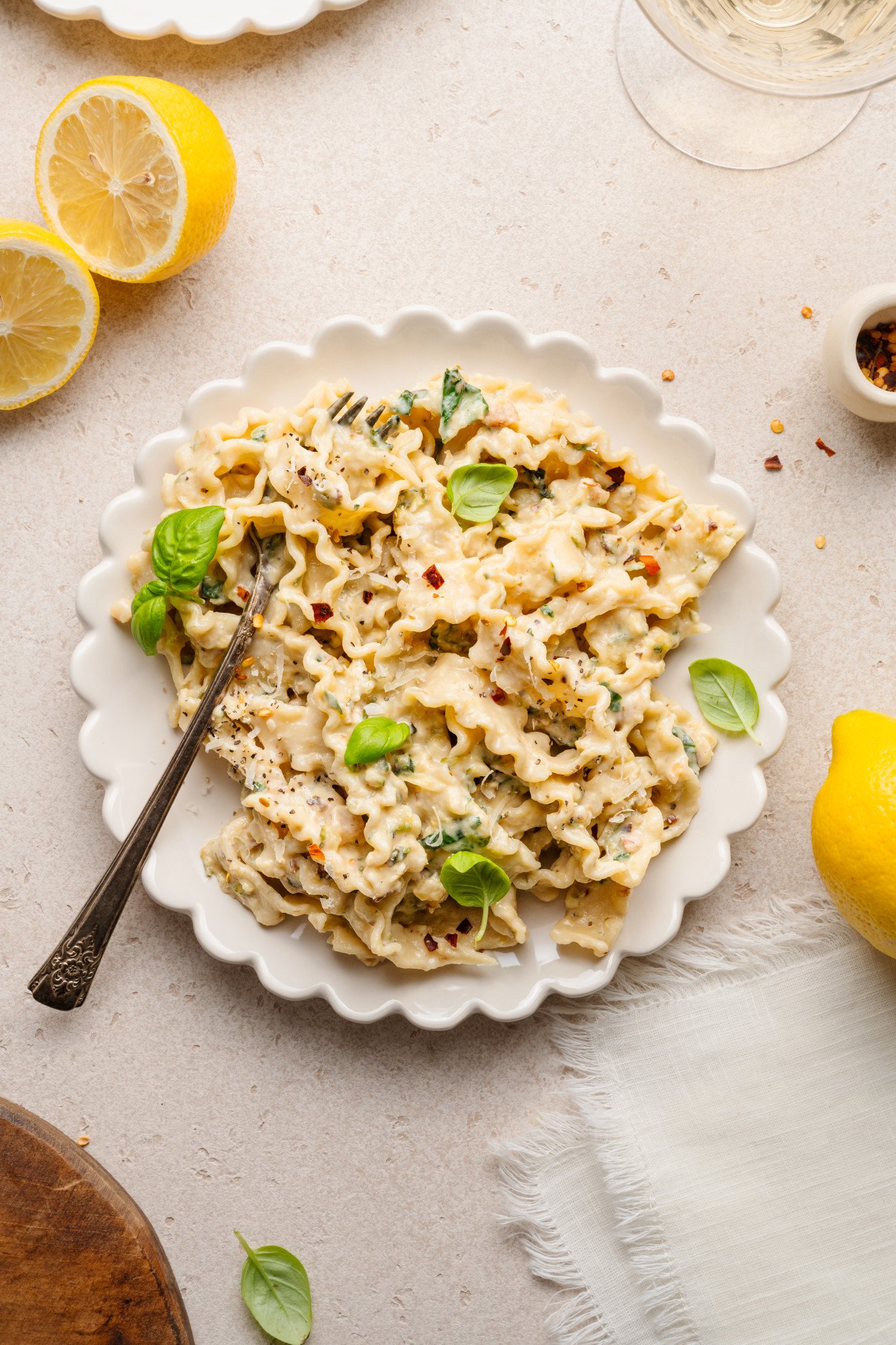 Zucchini lemon pasta garnished with basil in white scalloped bowl with fork.