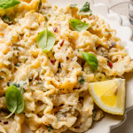 Zucchini lemon pasta garnished with fresh basil and lemon in white scalloped bowl.