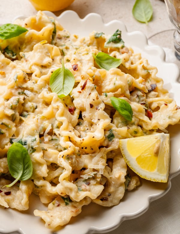 Zucchini lemon pasta garnished with fresh basil and lemon in white scalloped bowl.