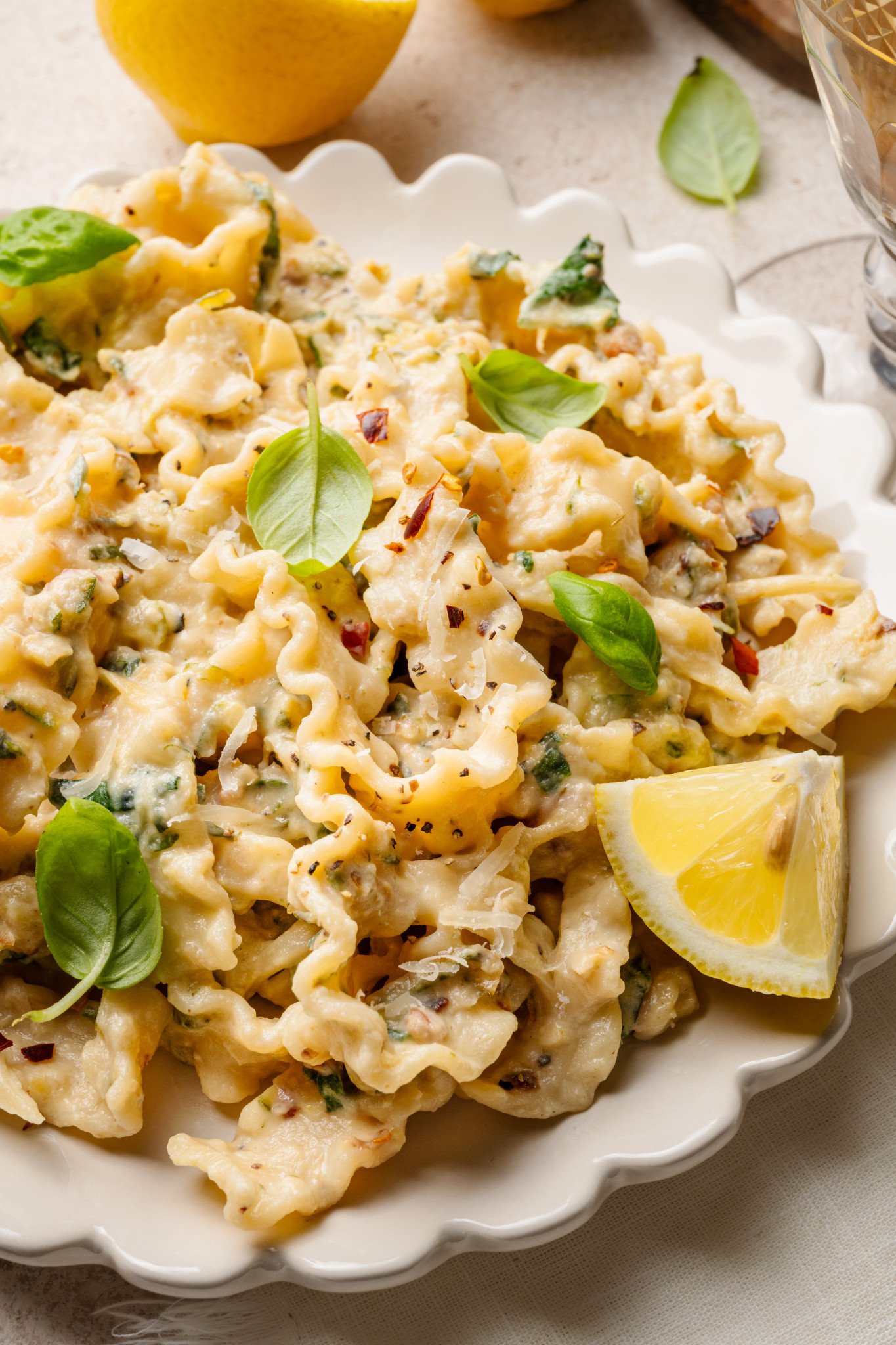 Zucchini lemon pasta garnished with fresh basil and lemon in white scalloped bowl.