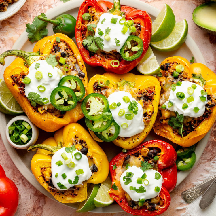Colorful medley of cooked stuffed peppers in a baking dish with bubbly melted cheese and visible bits of corn and black beans.