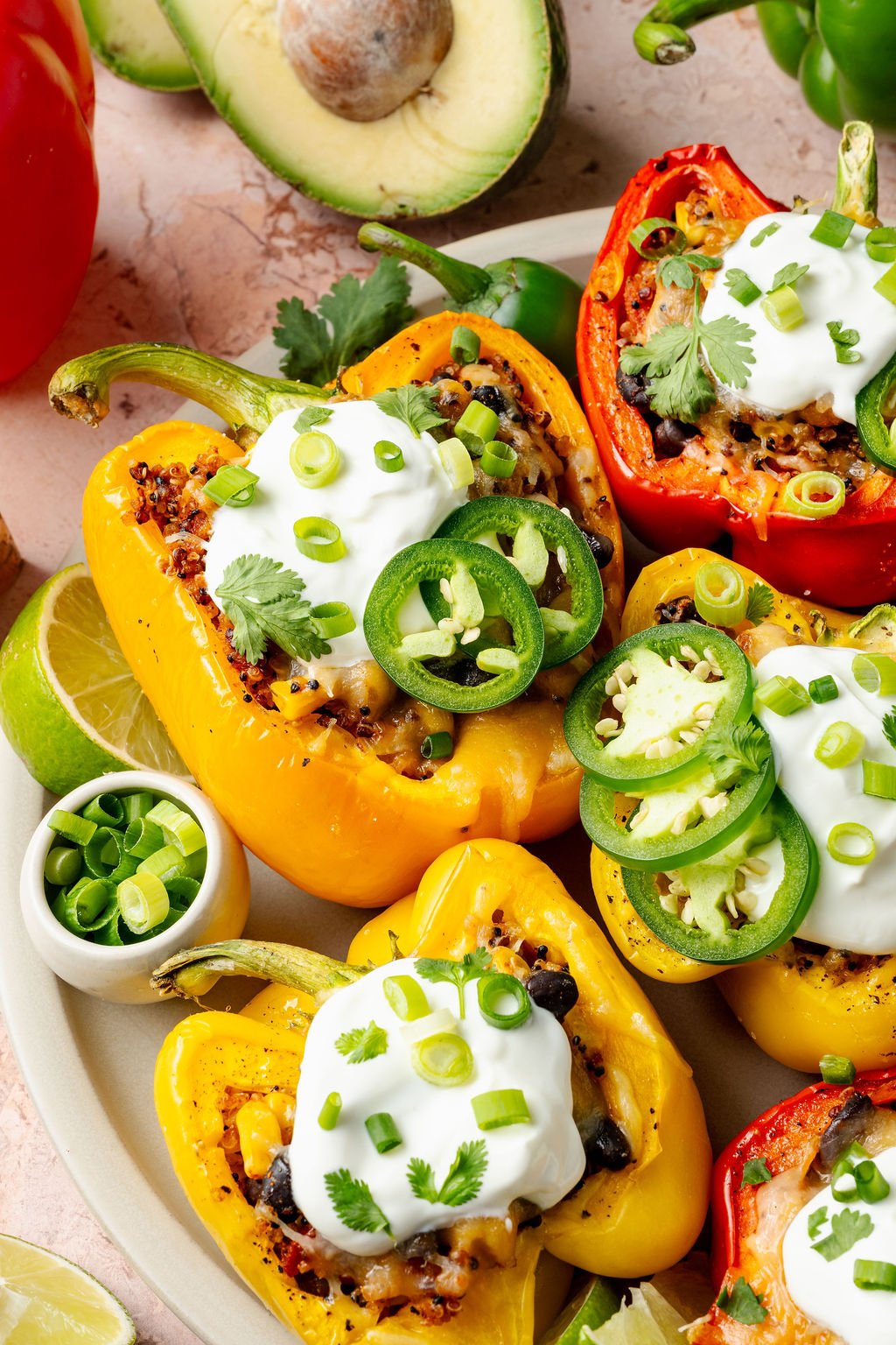 Side angle of a baked red pepper overflowing with a colorful quinoa filling, garnished with a scoop of sour cream and sliced green onions.