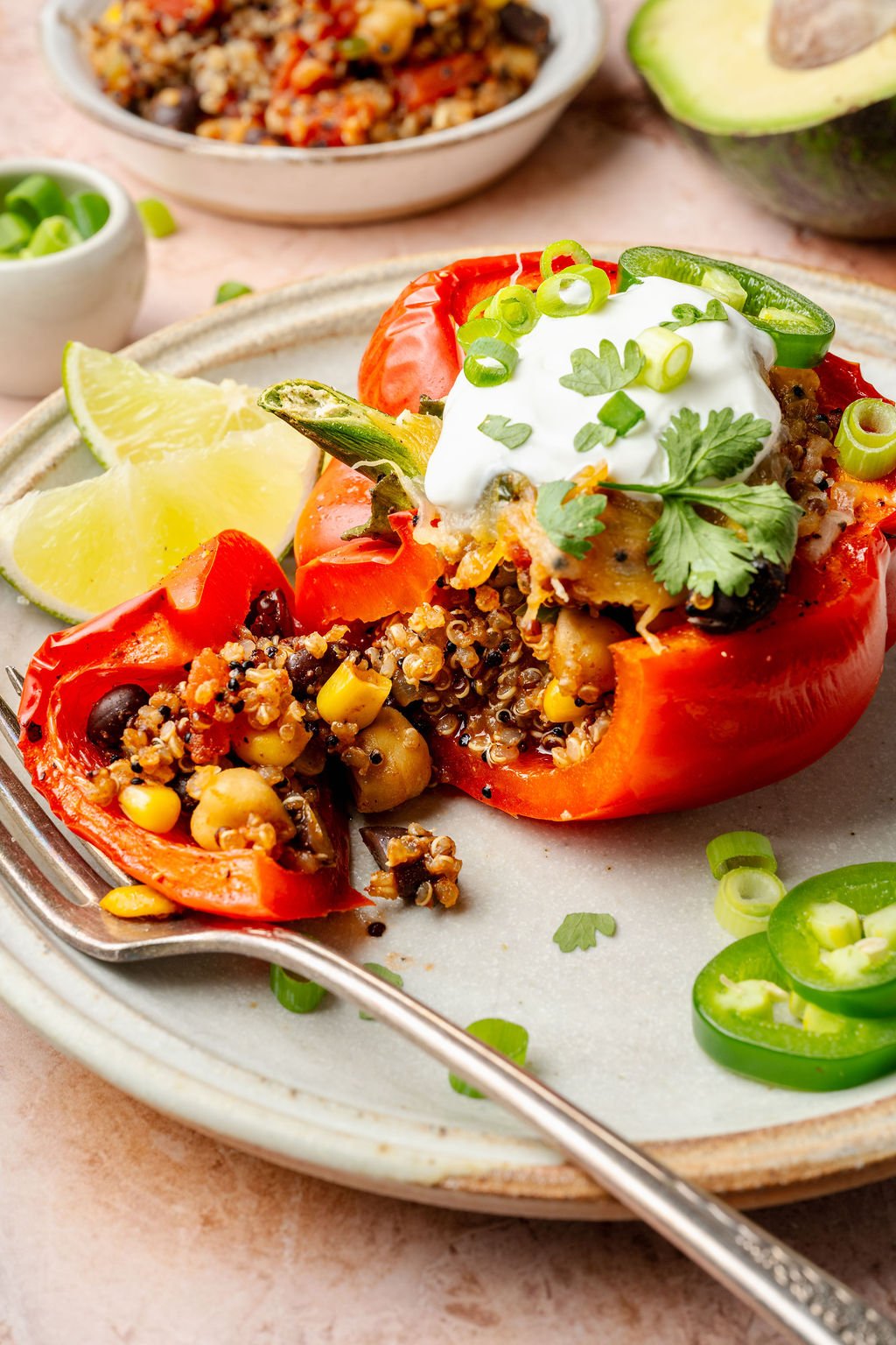 Close-up of a red bell pepper half filled with quinoa, beans, corn, and cheese, with visible seasoning and a rustic texture.