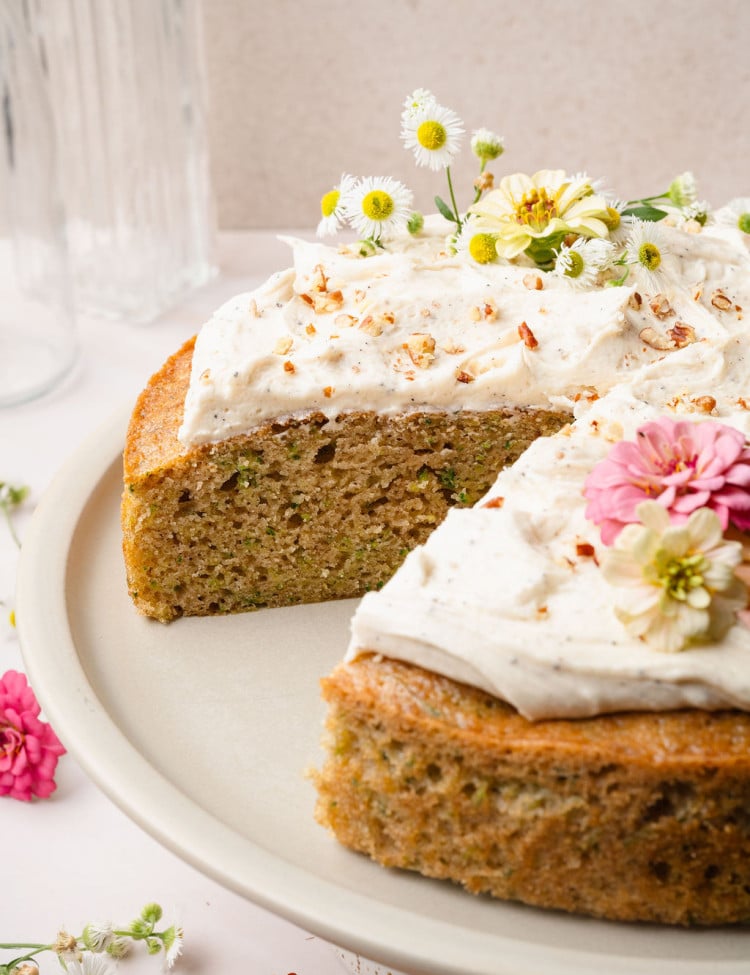Close-up of a frosted zucchini cake with a prominent view of the flower decorations and moist texture of the sliced cake layer.
