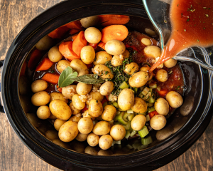 Adding the broth mixture on top of the beef and vegetables in the slow cooker.