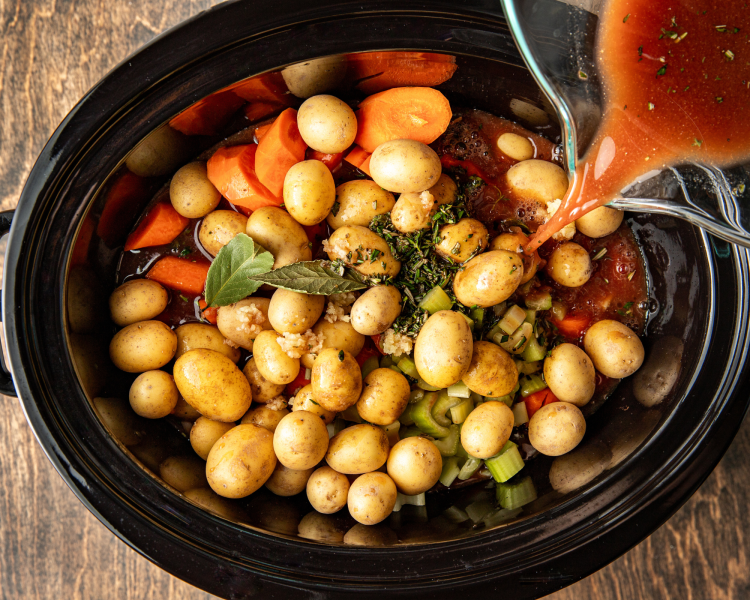 Adding the broth mixture on top of the beef and vegetables in the slow cooker.