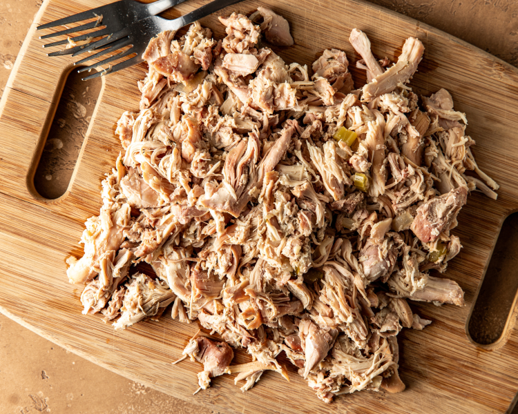 Chicken shredded into tiny pieces with two forks on wood cutting board.